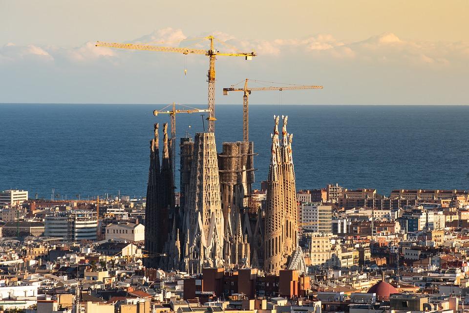 La imagen muestra el Templo Expiatorio de la Sagrada Familia en Barcelona. La fotografía es aérea, mostrando la Sagrada Familia desde la altura dominando la ciudad de Barcelona.
